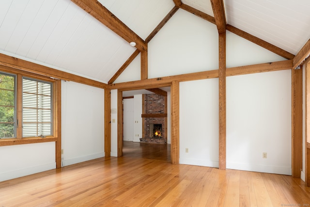 unfurnished living room with high vaulted ceiling, a brick fireplace, beam ceiling, and light wood-type flooring