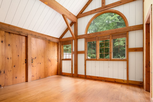 spare room featuring high vaulted ceiling, wooden walls, and light hardwood / wood-style floors