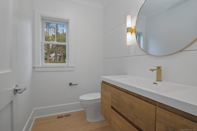 bathroom featuring wood-type flooring, vanity, ornamental molding, and toilet