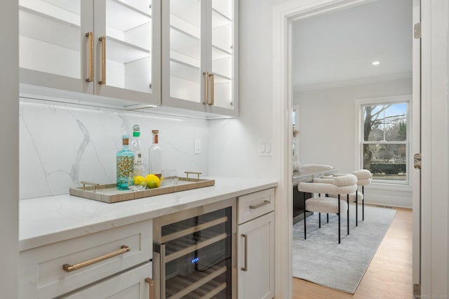 bar with light stone countertops, beverage cooler, tasteful backsplash, light hardwood / wood-style flooring, and crown molding