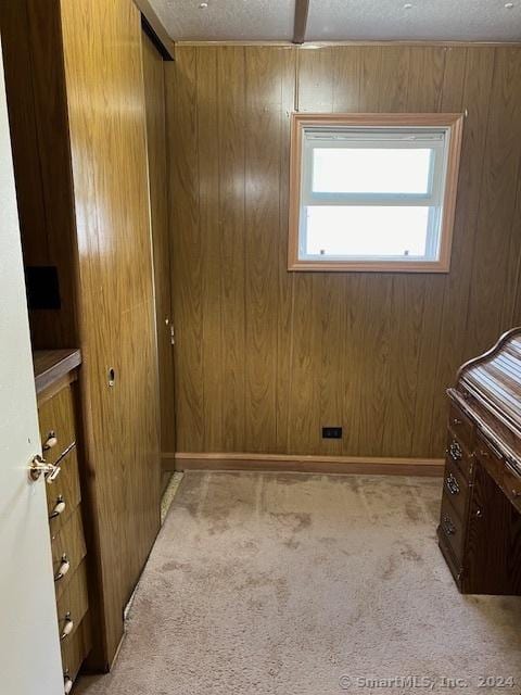 unfurnished room with a textured ceiling, light colored carpet, and wood walls