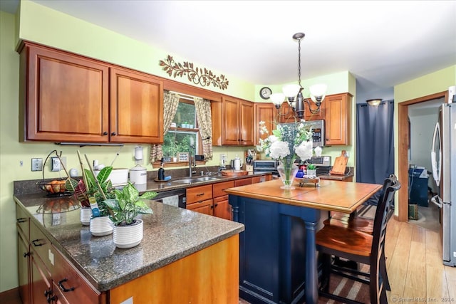 kitchen with sink, a kitchen island, stainless steel appliances, a notable chandelier, and light hardwood / wood-style floors