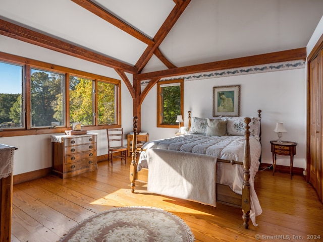 bedroom featuring multiple windows, beamed ceiling, and light hardwood / wood-style flooring