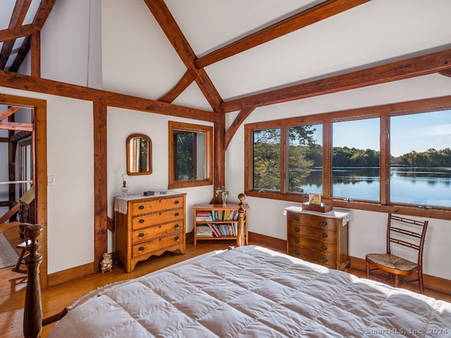 bedroom with lofted ceiling with beams, hardwood / wood-style floors, and a water view