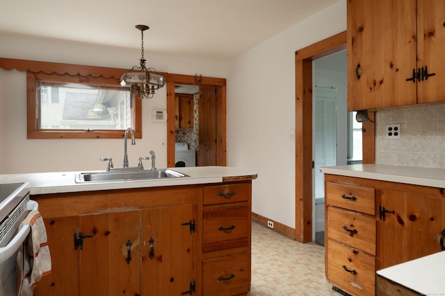 kitchen featuring washer / clothes dryer, tasteful backsplash, pendant lighting, sink, and a chandelier