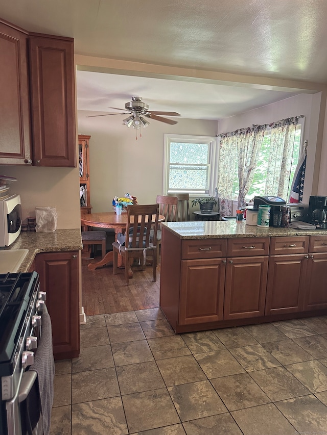 kitchen featuring light stone countertops, ceiling fan, stainless steel range, and dark wood-type flooring