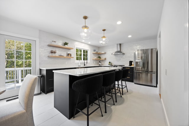 kitchen with stainless steel fridge with ice dispenser, a kitchen bar, hanging light fixtures, a kitchen island, and wall chimney exhaust hood