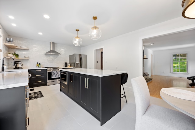 kitchen with a breakfast bar area, sink, hanging light fixtures, wall chimney exhaust hood, and stainless steel appliances