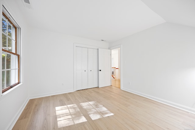 unfurnished bedroom featuring light hardwood / wood-style flooring, vaulted ceiling, and a closet