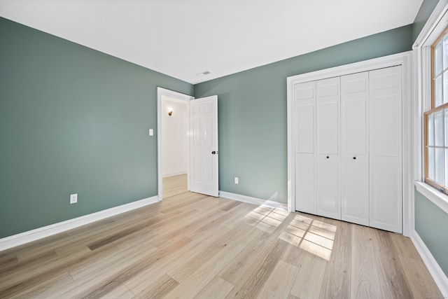 unfurnished bedroom with a closet, light hardwood / wood-style floors, and multiple windows