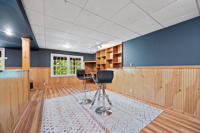 game room featuring ornate columns, wooden walls, light wood-type flooring, and a drop ceiling