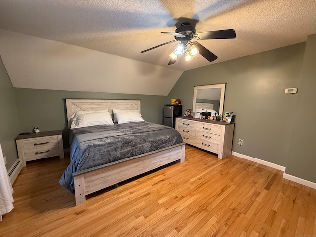 bedroom featuring ceiling fan, baseboard heating, light hardwood / wood-style flooring, vaulted ceiling, and a textured ceiling