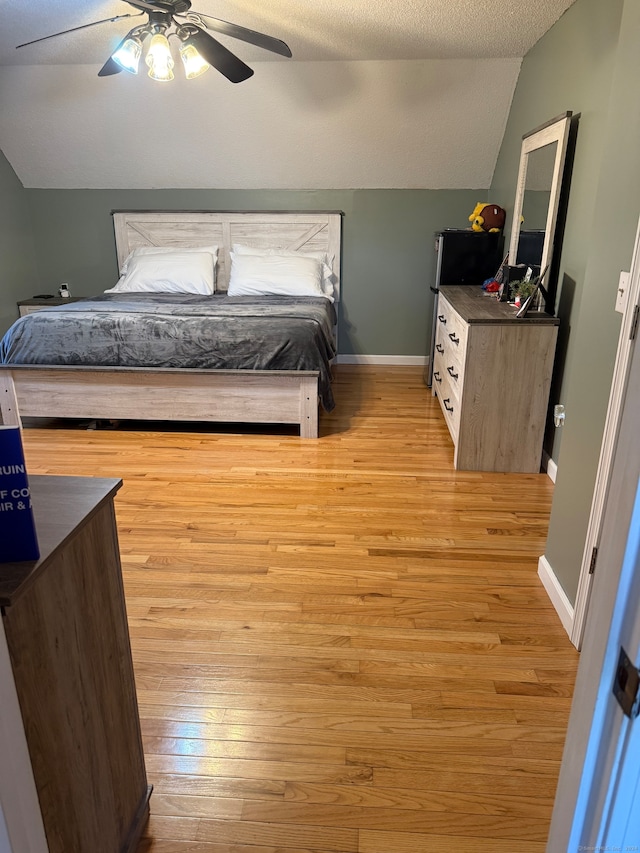 bedroom with ceiling fan, light wood-type flooring, a textured ceiling, and vaulted ceiling