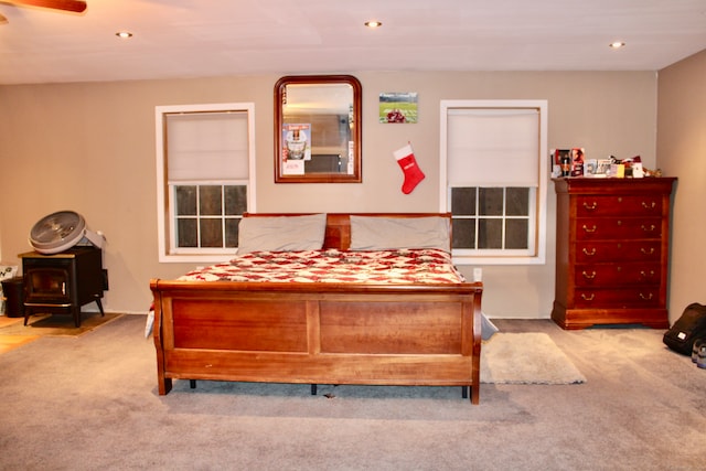 bedroom featuring ceiling fan, light colored carpet, and a wood stove