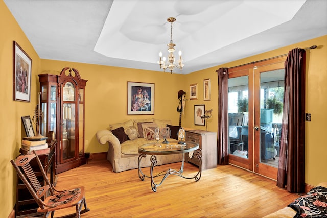 living room with a tray ceiling, light hardwood / wood-style flooring, french doors, and a notable chandelier