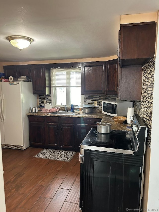 kitchen with dark wood-type flooring, tasteful backsplash, white appliances, dark brown cabinets, and sink