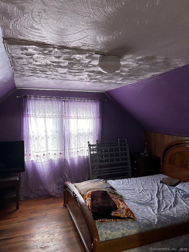 bedroom featuring vaulted ceiling, a textured ceiling, and hardwood / wood-style floors