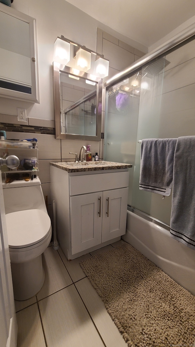 full bathroom featuring tile walls, tile patterned floors, vanity, enclosed tub / shower combo, and toilet