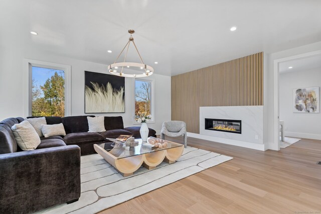 living room featuring plenty of natural light, light hardwood / wood-style floors, a premium fireplace, and a chandelier