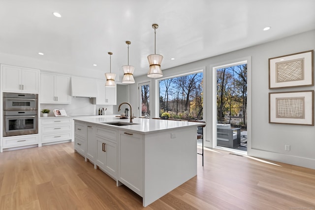 kitchen with white cabinets, double oven, hanging light fixtures, and sink