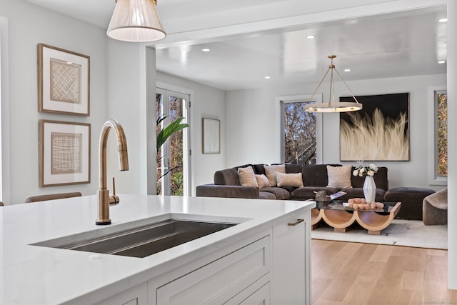 kitchen with pendant lighting, white cabinets, sink, light stone countertops, and light wood-type flooring