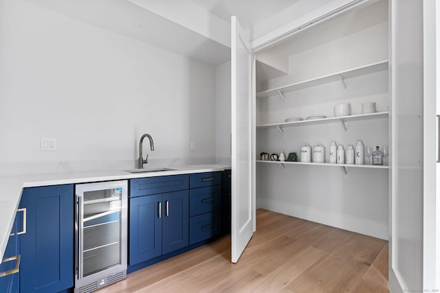 bar featuring blue cabinets, light wood-type flooring, sink, and beverage cooler