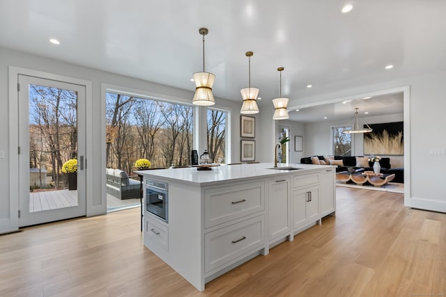 kitchen with a kitchen island with sink, white cabinets, hanging light fixtures, and light wood-type flooring