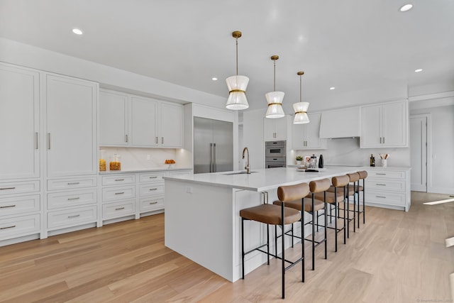 kitchen featuring white cabinetry, an island with sink, stainless steel appliances, and light wood-type flooring