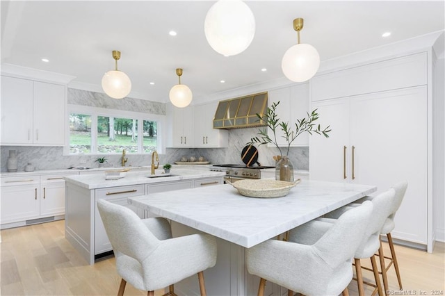 kitchen with white cabinets, a kitchen island, light hardwood / wood-style flooring, decorative light fixtures, and wall chimney range hood