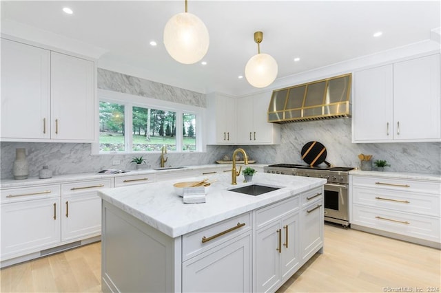 kitchen with white cabinets, hanging light fixtures, sink, high end range, and wall chimney exhaust hood