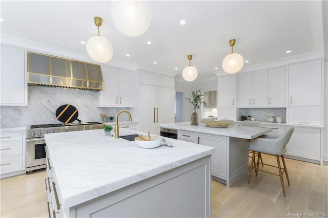 kitchen featuring pendant lighting, an island with sink, wall chimney exhaust hood, white cabinetry, and high end stove