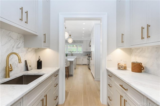 kitchen featuring light hardwood / wood-style floors, sink, light stone counters, and white cabinets