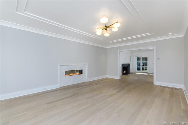 unfurnished living room featuring ornamental molding, a raised ceiling, a chandelier, and light hardwood / wood-style floors