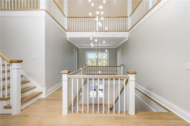 stairs with an inviting chandelier, wood-type flooring, a high ceiling, and crown molding