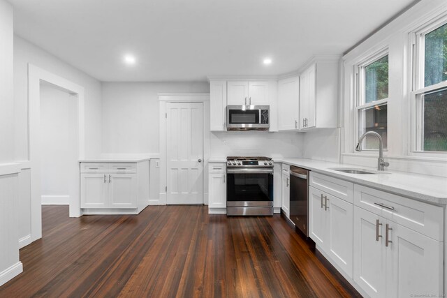 kitchen with light stone counters, white cabinets, sink, appliances with stainless steel finishes, and dark hardwood / wood-style floors