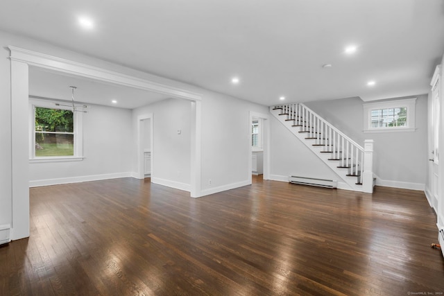 unfurnished living room featuring a chandelier, baseboard heating, dark wood-type flooring, and a wealth of natural light