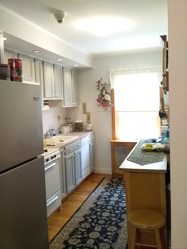 kitchen featuring white cabinets, sink, white appliances, light wood-type flooring, and a kitchen bar