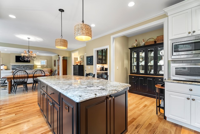 kitchen featuring white cabinets, light hardwood / wood-style floors, stainless steel microwave, and decorative columns