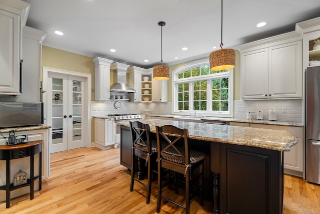 kitchen featuring pendant lighting, a center island, white cabinetry, wall chimney exhaust hood, and light hardwood / wood-style flooring