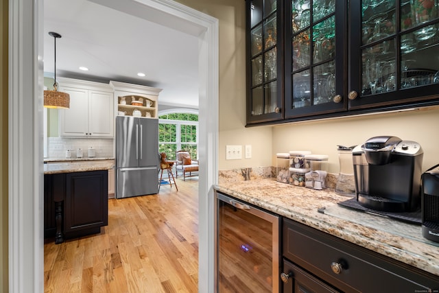 bar featuring light wood-type flooring, tasteful backsplash, white cabinetry, stainless steel refrigerator, and light stone countertops