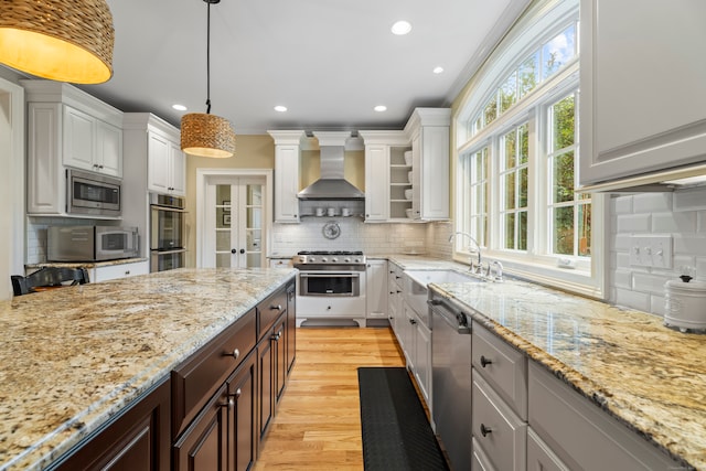 kitchen with decorative light fixtures, wall chimney range hood, stainless steel appliances, and white cabinets