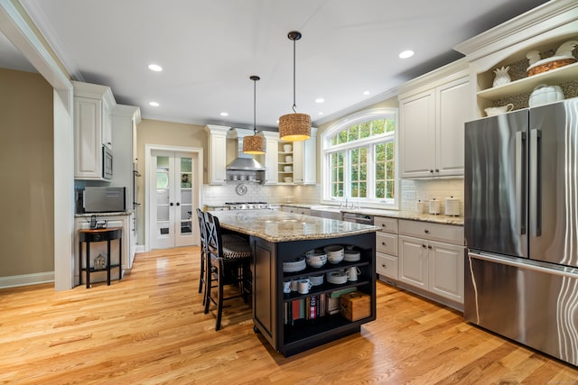 kitchen with stainless steel fridge, light hardwood / wood-style floors, a breakfast bar area, light stone countertops, and a center island