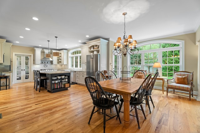 dining space with french doors, light wood-type flooring, crown molding, and a chandelier