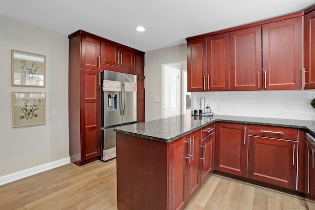 kitchen featuring reddish brown cabinets, stainless steel refrigerator with ice dispenser, dark stone countertops, light wood-type flooring, and a peninsula