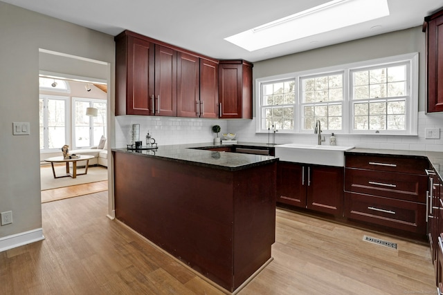 kitchen with a skylight, decorative backsplash, light wood-style floors, and dark brown cabinets