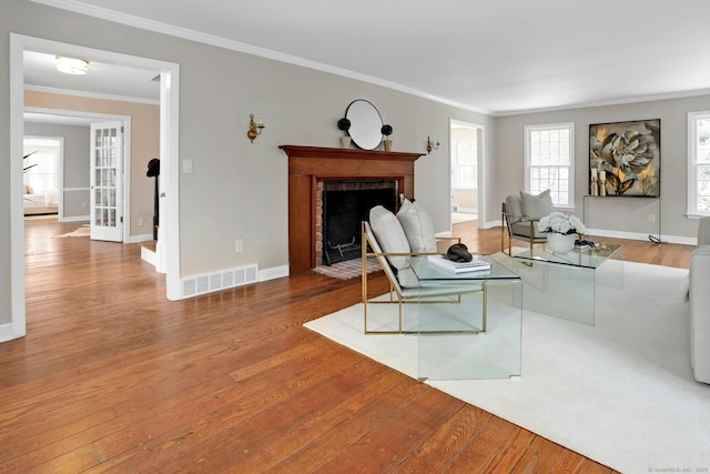 living room with a fireplace with flush hearth, visible vents, crown molding, and wood finished floors