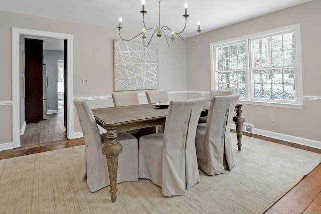 dining space with baseboards, visible vents, an inviting chandelier, and wood finished floors