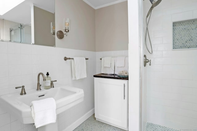 bathroom with tile walls, ornamental molding, wainscoting, a sink, and a shower stall