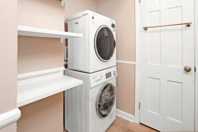 clothes washing area with light tile patterned floors, laundry area, baseboards, and stacked washer / drying machine