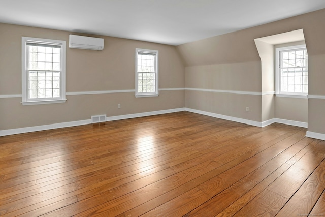 bonus room featuring visible vents, hardwood / wood-style floors, vaulted ceiling, a wall mounted air conditioner, and baseboards